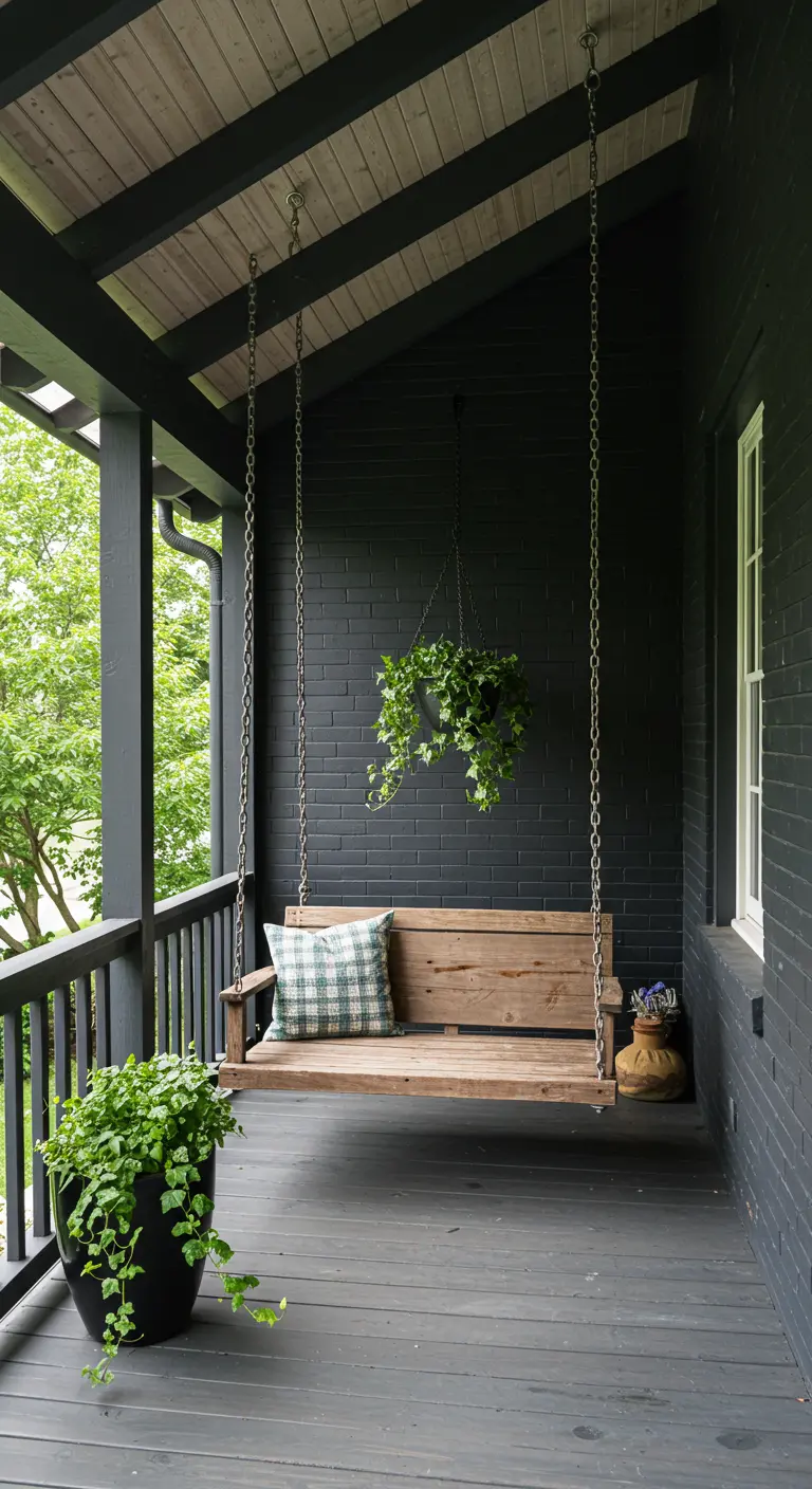 Porche pintado de negro con un columpio de madera y plantas colgantes, creando un ambiente acogedor.