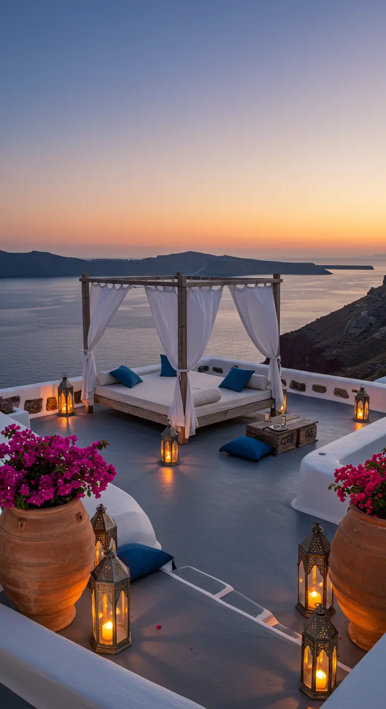 Cama balinesa blanca con cortinas y cojines azules en una terraza con vistas al mar al atardecer.