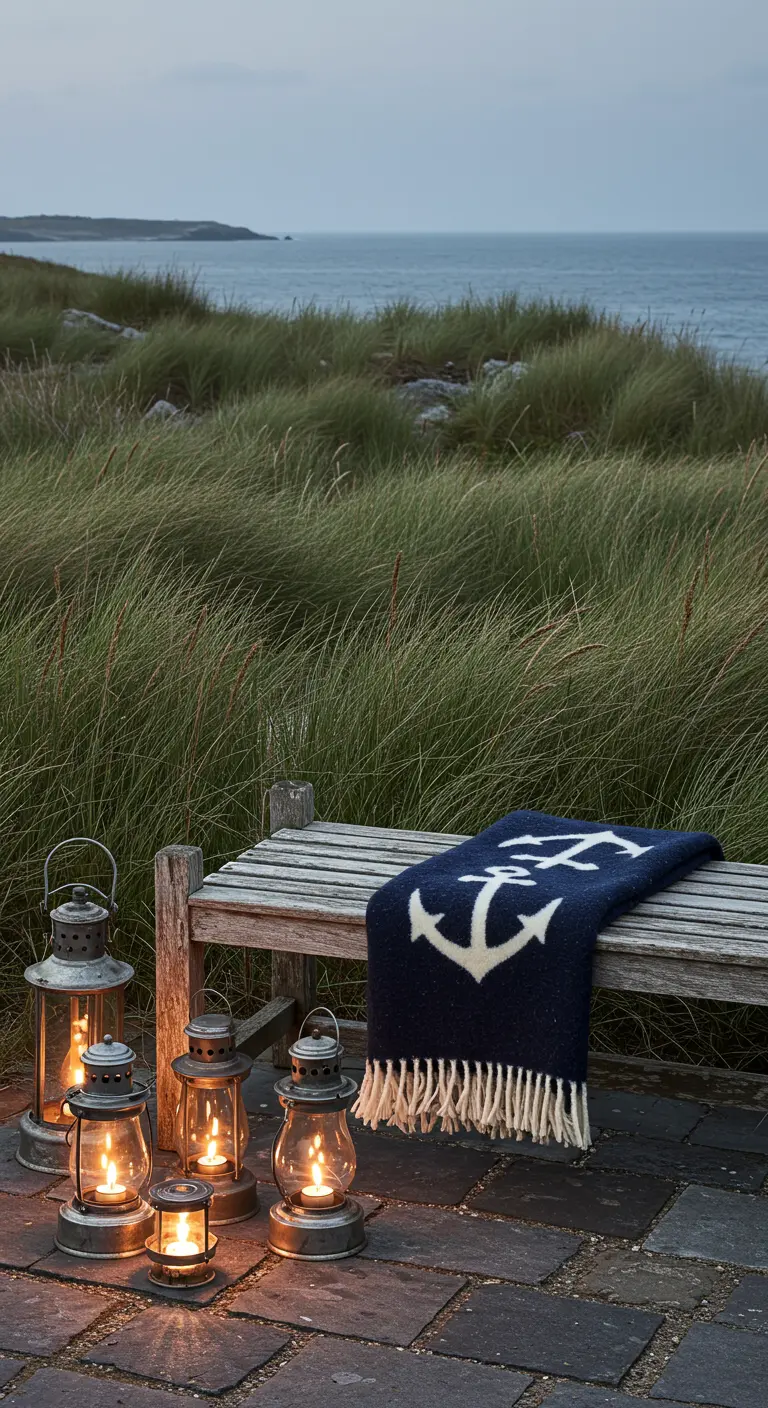 Banco de madera junto al mar con dunas, una manta azul con un ancla y un grupo de faroles de tormenta.