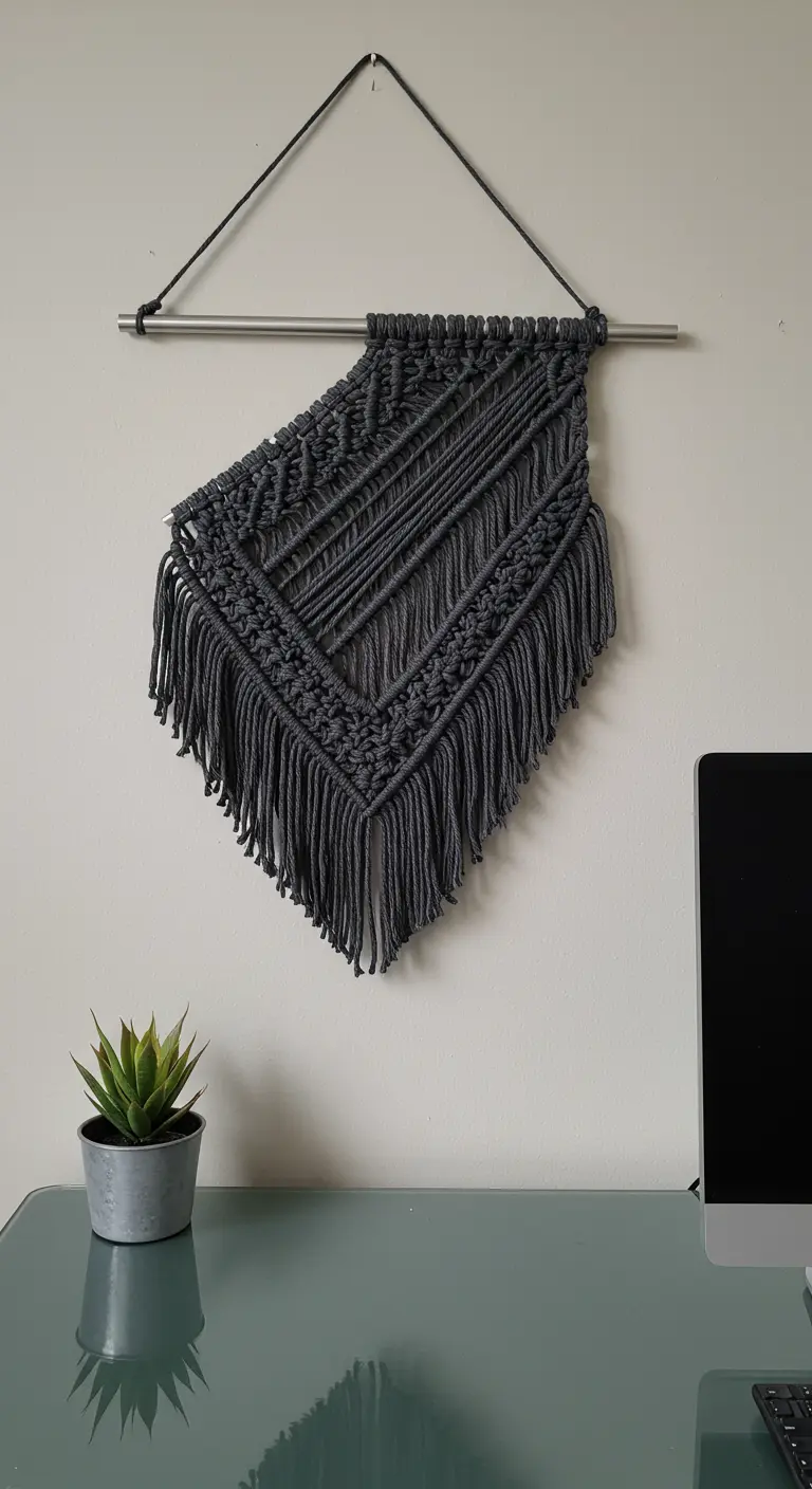 Tapiz de macramé asimétrico en color gris oscuro colgado de una barra metálica.