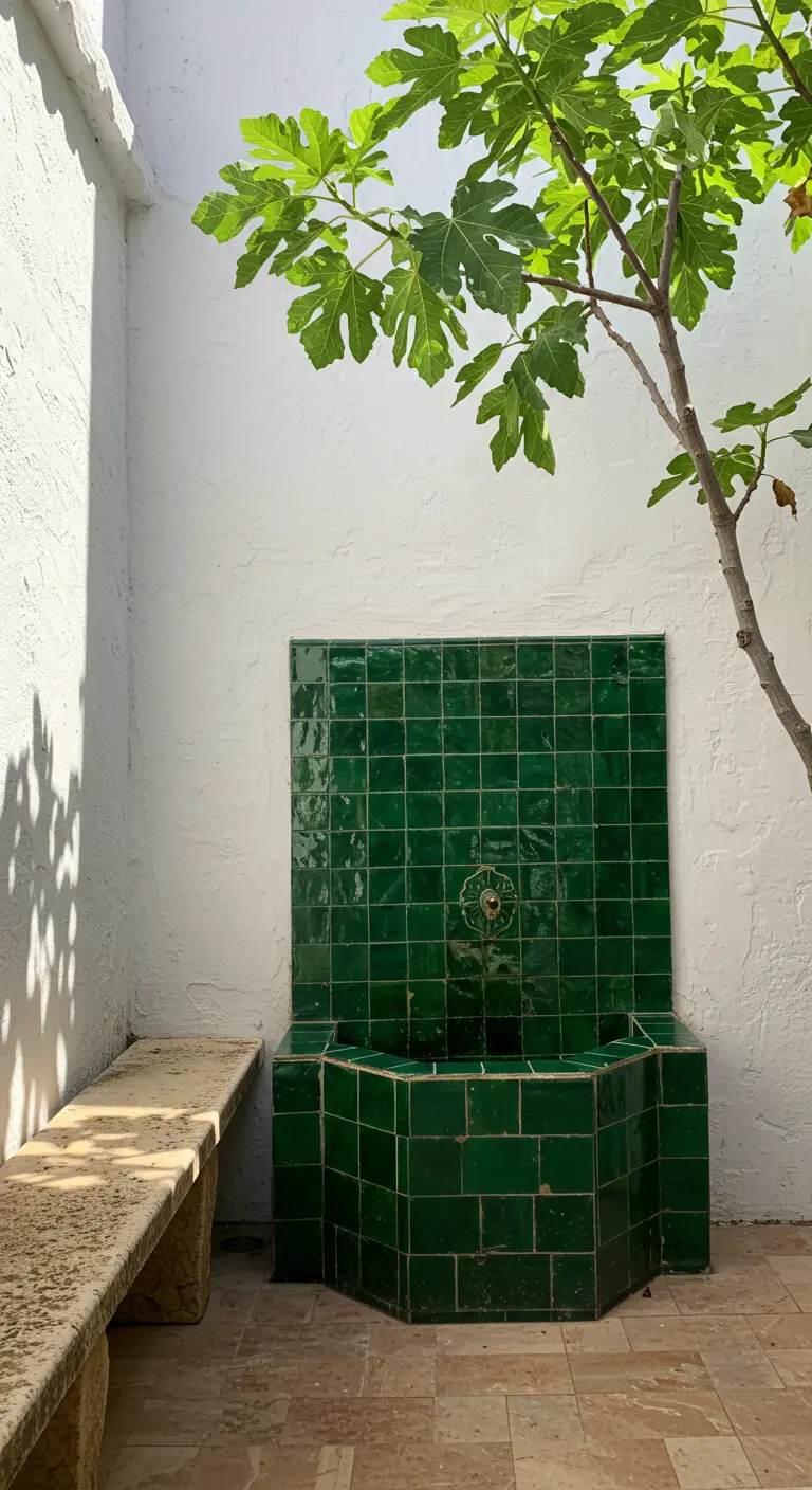 Fuente de pared con azulejos verdes vidriados junto a un banco de piedra y una higuera