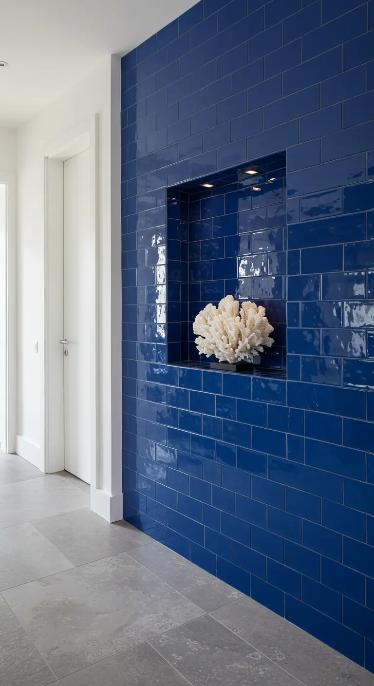 Pared de azulejos de metro en color azul cobalto con un nicho iluminado que exhibe un coral blanco.