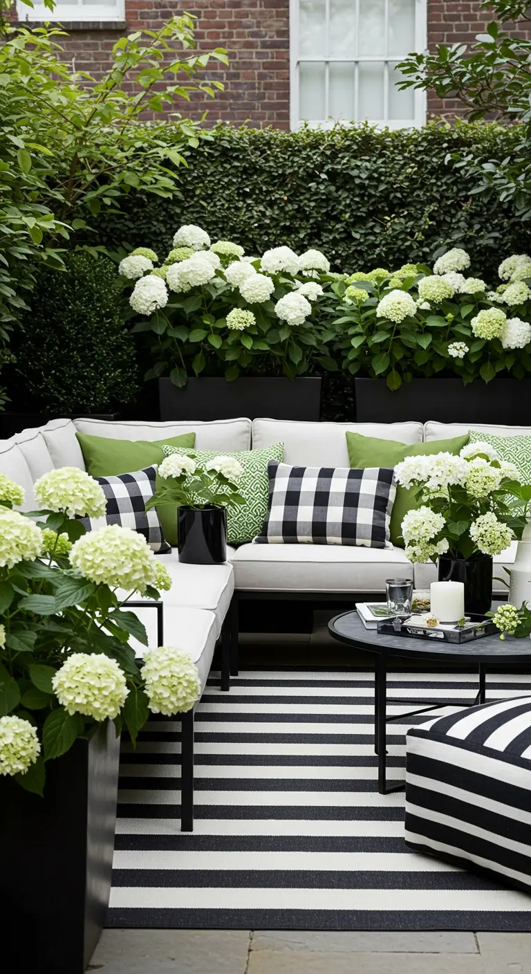 Patio elegante en blanco y negro con un sofá seccional, alfombra de rayas y hortensias blancas.