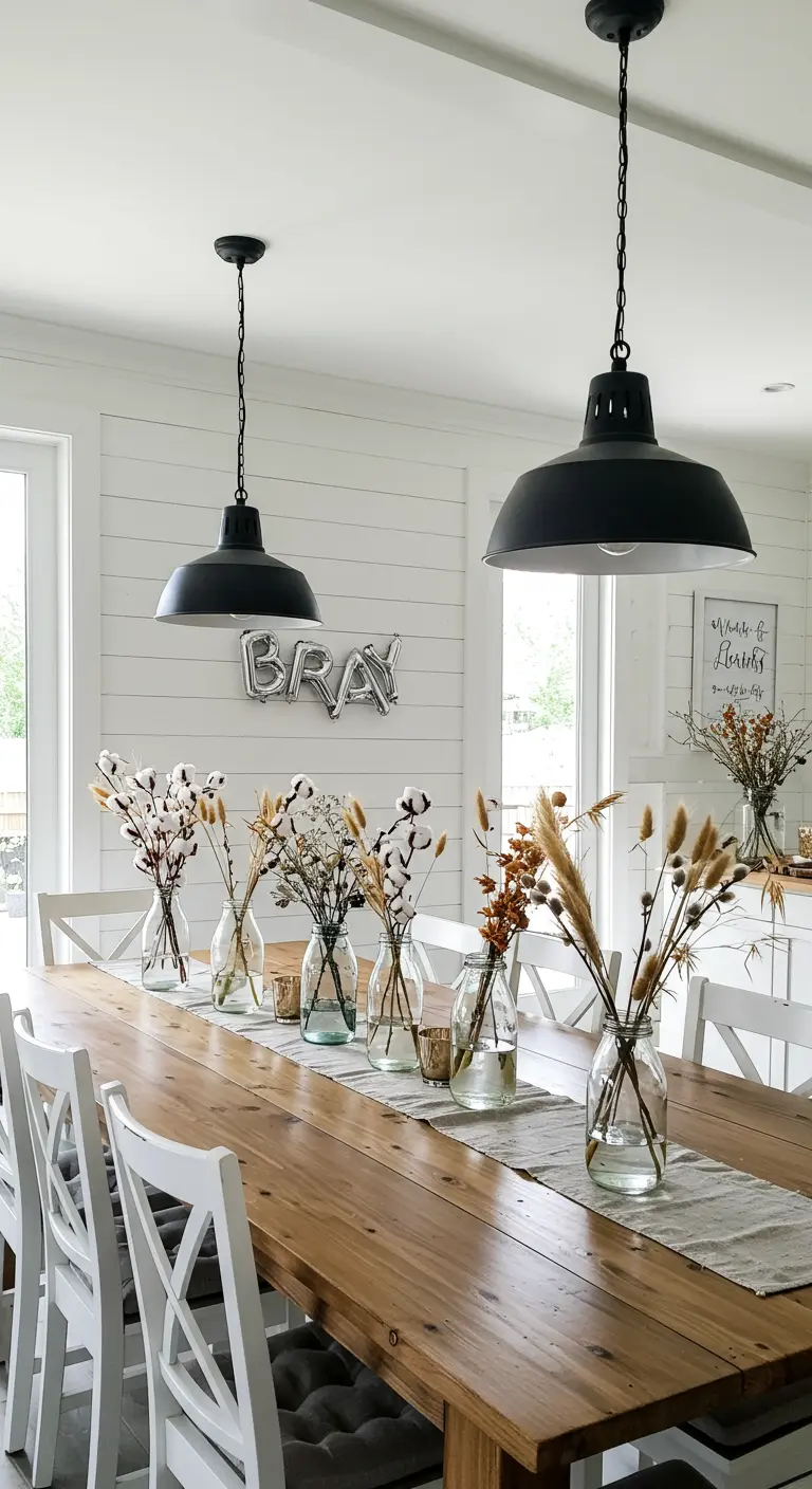Mesa de comedor de madera en un interior blanco con centros de mesa de flores de algodón y trigo.
