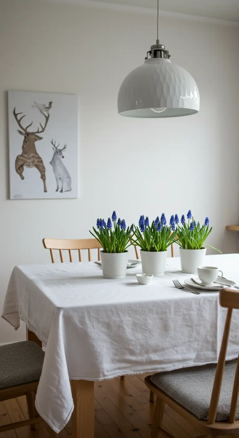 Mesa de comedor escandinava con mantel blanco y jacintos de uva azules en macetas.