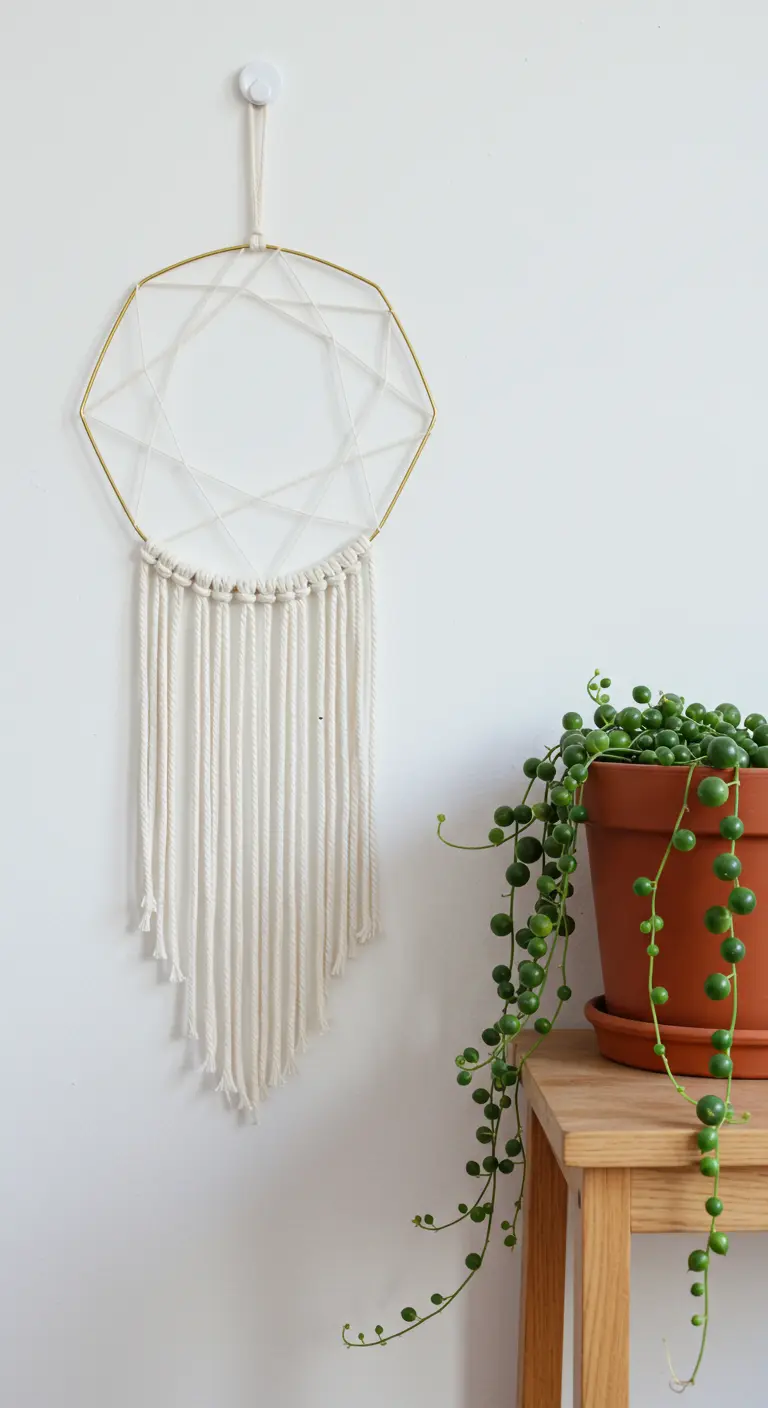 Atrapasueños minimalista con aro dorado geométrico y flecos de macramé blanco.