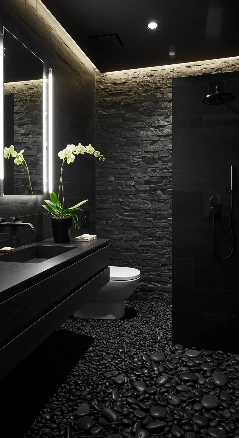 Baño completamente negro con pared de piedra, suelo de cantos rodados y una orquídea blanca.