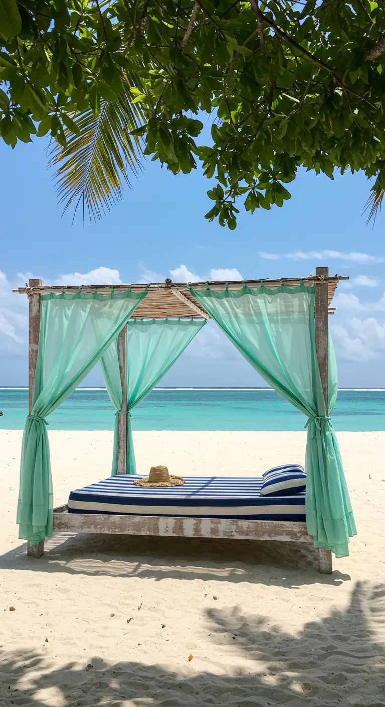 Cama balinesa de madera clara con cortinas turquesas en una playa de arena blanca.