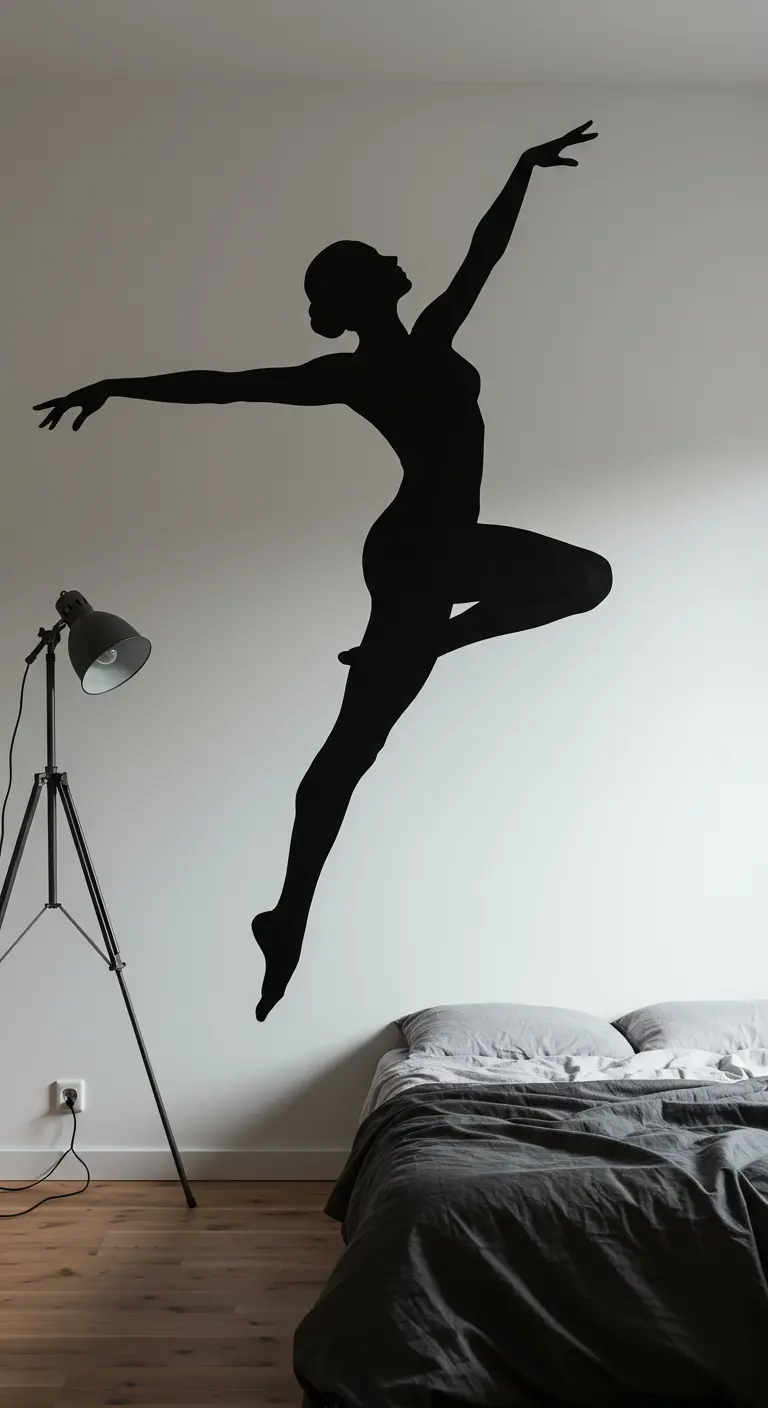 Silueta negra de una bailarina pintada en una pared blanca, sobre una cama con sábanas grises.