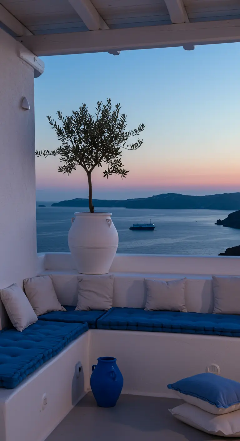 Balcón blanco de estilo griego con banco de obra, cojines azules y un gran olivo en una maceta.