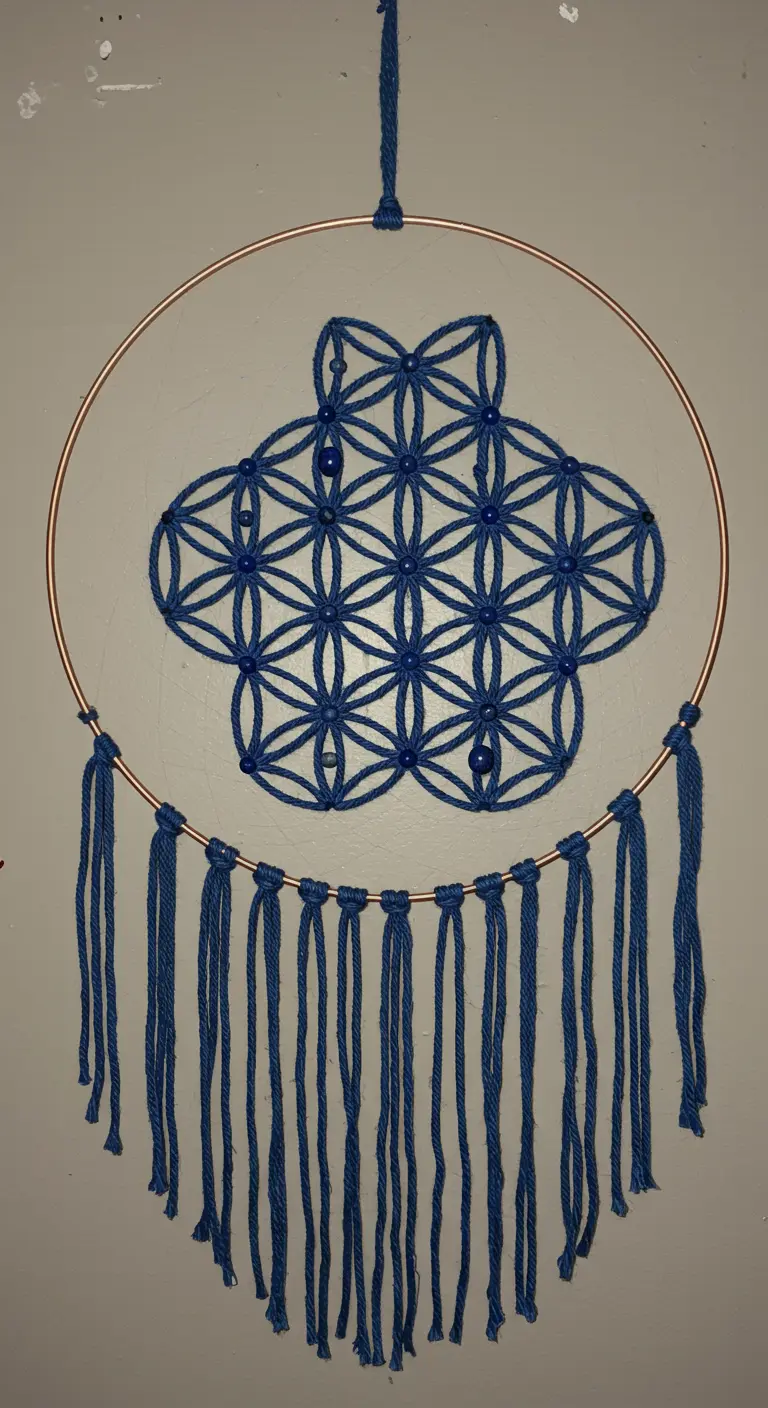 Atrapasueños con un patrón tejido de la Flor de la Vida en hilo azul sobre un aro de cobre.