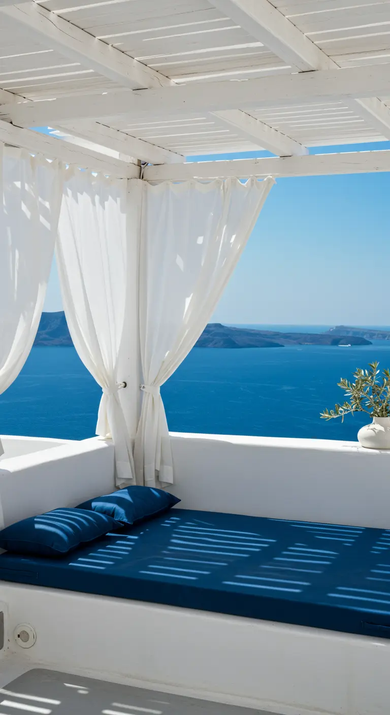 Cama de obra blanca con colchón azul y cortinas blancas en un balcón con vistas al mar.