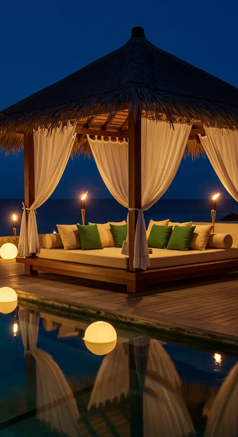 Cama balinesa con cortinas blancas y cojines verdes junto a una piscina con luces flotantes esféricas.
