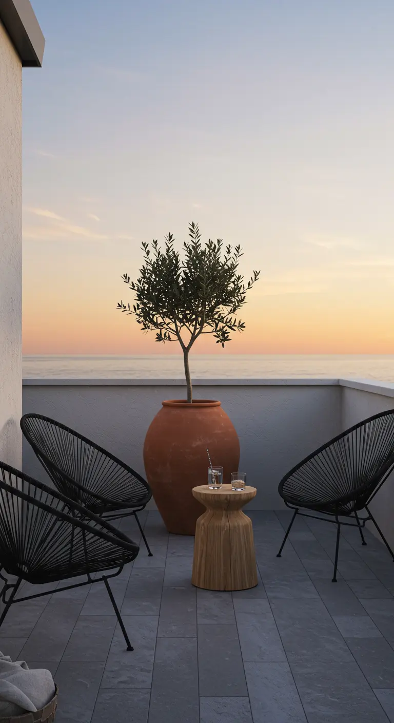 Balcón con vistas al mar, un olivo en maceta de terracota y sillas negras de diseño.