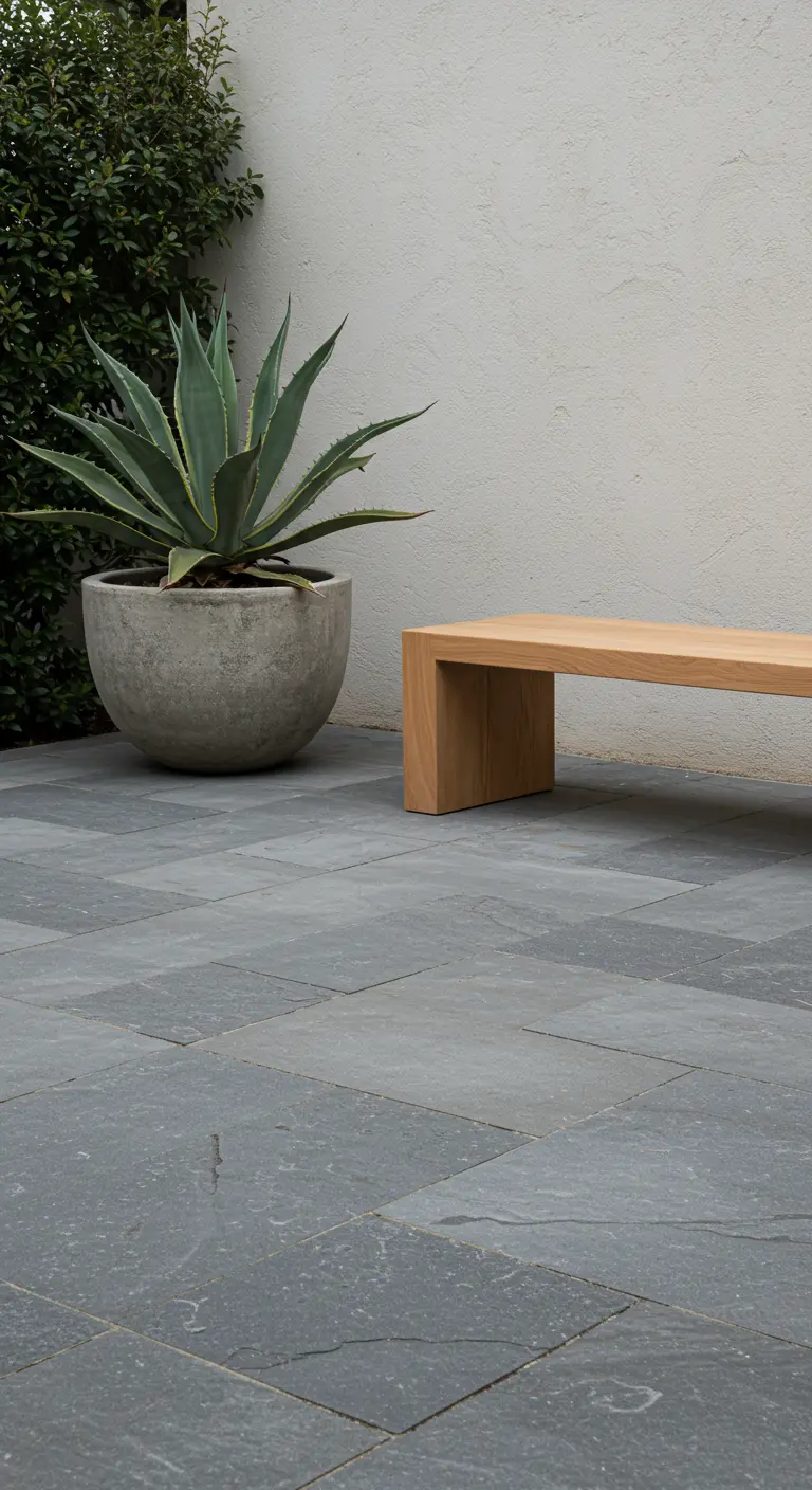 Patio minimalista con suelo de pizarra, un banco de madera de líneas rectas y un gran agave en maceta de cemento.