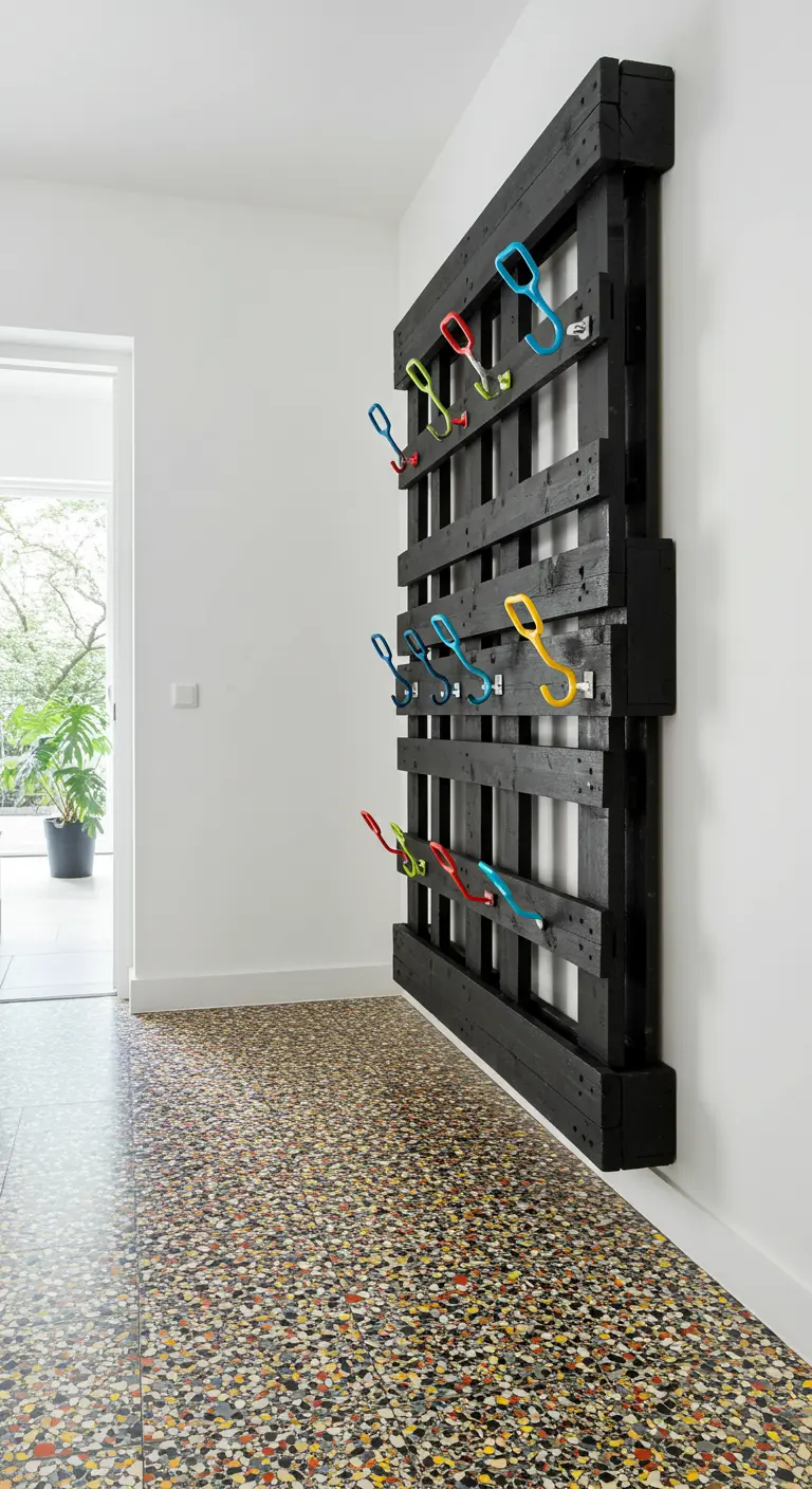 Perchero de pared hecho con un palet pintado de negro y ganchos de colores vivos.
