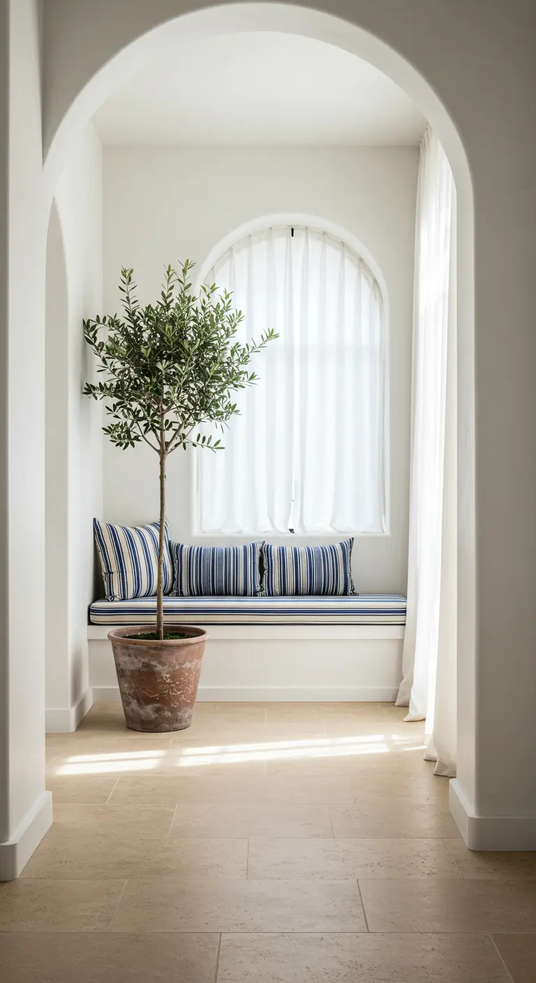Rincón acogedor bajo un arco con un banco, cojines de rayas azules y blancas y un olivo en maceta